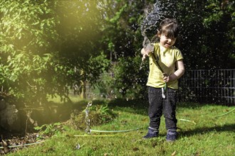 Blurred background of girl playing with water hose outdoors in garden in backyard at home on sunny day