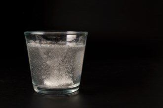 Close-up of a effervescent tablet in a glass of water on a black background with copy space