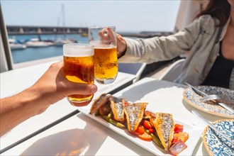 A couple toasting with beer by the sea eating fried fish