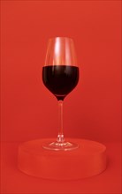 Glass of red wine on the podium. Red bright background. Minimalism. Close up. Copy space. Valentines Day concept. Mockup for holidays design