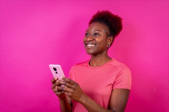 Young african american woman isolated on a pink background smiling with the mobile phone