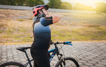 Sporty cyclist having neck pain while riding a bike. Male cyclist with neck pain outdoors
