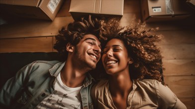 Happy young adult couple laying on the floor of their new home with moving boxes surrounding them