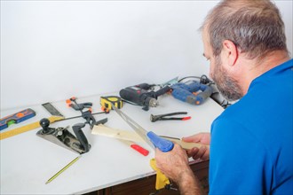 Rear view of a male carpenter cutting wood in his workshop with a saw in the background with various tools on the table