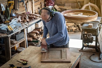 Carpenter sanding a wood with an orbital sander in a workshop