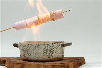 Marshmallows skewered in the fire of a ceramic bowl on a wooden board