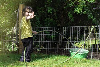 Happy little girl playing with a garden hose waving at the camera. Outdoor activity for kids