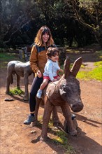 A boy and a mother playing on the wooden horse in the leisure area at Laguna Grande in the Garajonay natural park on La Gomera