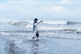 Fisherman walking with his net into the sea looking at the camera