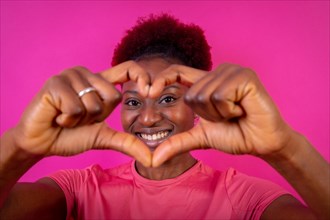 Young african american woman isolated on a pink background smiling and heart gesture