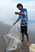 A rustic Central American fisherman with moustaches and curly hair prepares his net on the seashore. Vertical portrait