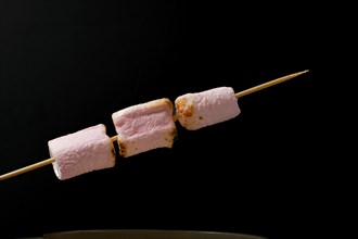 Roasted marshmallows on a skewer isolated on black background and copy space