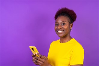 Young african american woman isolated on a purple background smiling with the mobile phone