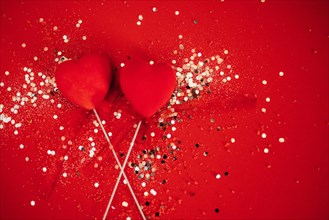 Two decorative hearts on a stick with ribbon. Bright background with silver sequins and round confetti. Sovereign velvet hearts on a red backdrop. Copy space. Valentine day concept