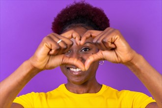Young african american woman isolated on a purple background smiling and heart gesture