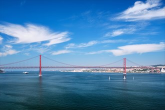 View of 25 de Abril Bridge famous tourist landmark of Lisbon connecting Lisboa to Almada on Setubal Peninsula over Tagus river with boats yachts and vessels. Lisbon