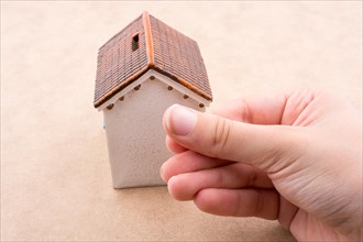 Little model house and a hand on a light brown color background