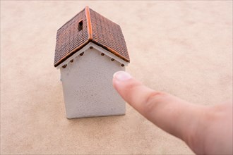 Little model house and a hand on a light brown color background