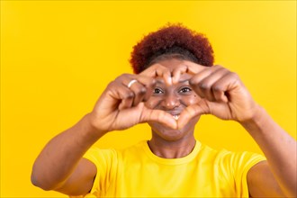 Young african american woman isolated on a yellow background smiling and heart gesture