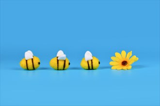 Felt bees in a row crawling towards yellow flower on blue background with copy space