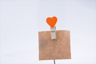 Heart shape clothespin attached to a note paper on a white background