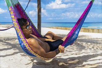 Handsome man relaxing in a hammock with Caribbean Sea in the background. Concept Vacation