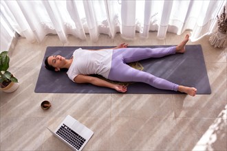 Young woman in a yoga studio meditating and listening to relaxing music in Shavasana pose