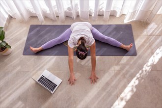 Overhead shot of woman practicing yoga online with a computer in a bright room