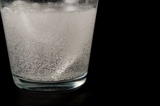 Close-up of a effervescent tablet in a glass of water on a black background with copy space