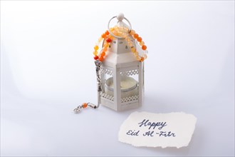 The word EID EL FITR on torn paper beside a lantern and prying beads