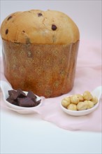 Panettone on a pink cloth and white background with ceramic spoons with hazelnuts and chocolate