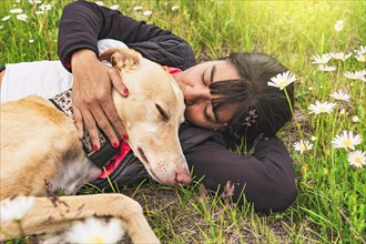 Relaxed woman kissing her pet outdoors surrounded by flowers. Pet owner with her greyhound