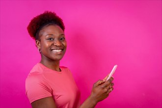 Young african american woman isolated on a pink background smiling with the mobile phone