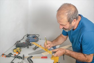 Front view of a bearded carpenter measuring a timber with a tape measure in his home workshop