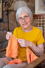 70s grandmother looking at camera enjoying knitting at home