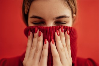 Portrait of young blondy girl in a red knitted sweater. Cute female teenager holding sweater collar with her hands. Close up of a beautiful bright red manicure