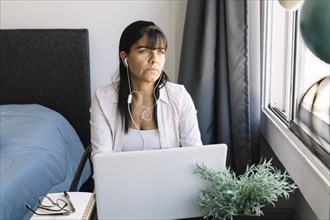 Latina woman working in her apartment looks towards window. Home office concept