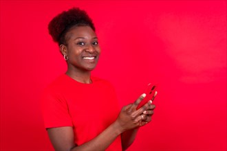 Young african american woman isolated on a red background smiling with the mobile phone