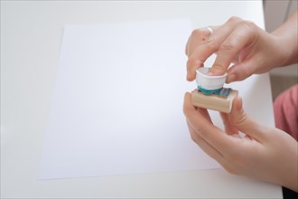 Woman's hands dipping a rubber stamp in ink in the background a blank sheet of paper for stamping the stamp