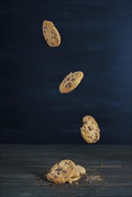 Chocolate cookies falling in a row on a wooden table with dark background and copy space