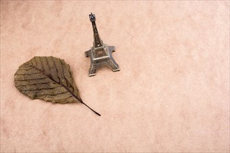 Little model Eiffel Tower and a dry leaf on brown background