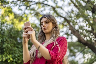 Low angle view of young blond woman using smartphone outdoors. Modern technologies concept