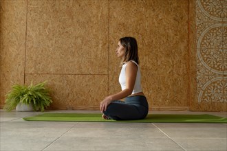 Relaxed young woman in a semi-lotus position on a green mat in a nice interior ready to meditate