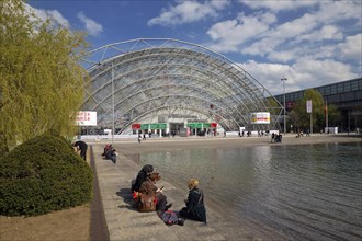 Glass hall with people at the water basin in front of the main entrance of the Leipzig Trade Fair