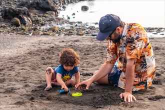 Father with his son playing on the black sand beach of Valle Gran Rey on La Gomera in summer