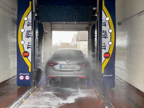 Rear view from behind of motor vehicle sporty sedan Italian make automobile Alfa Romeo Giulia being sprayed in car wash with car shampoo chemical care chemicals