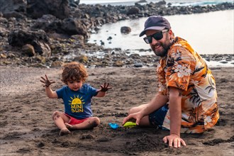 Portrait of father with his son playing on the black sand beach of Valle Gran Rey on La Gomera