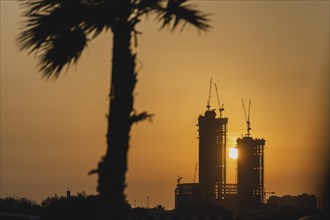 The sun sets behind two high-rise buildings under construction