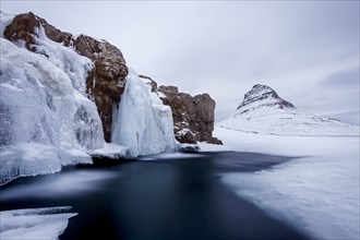 Kirkjufell mountain and the frozen waterfall Kirkjufellsfoss on the Snaefellsnes peninsula in the snow in winter