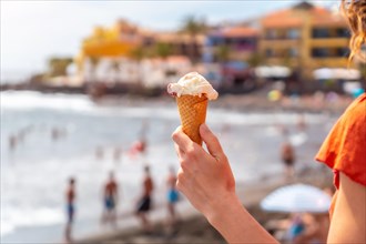 Hand of a tourist woman smiling with a hat eating an ice cream on the beach of Valle Gran Rey in La Gomera